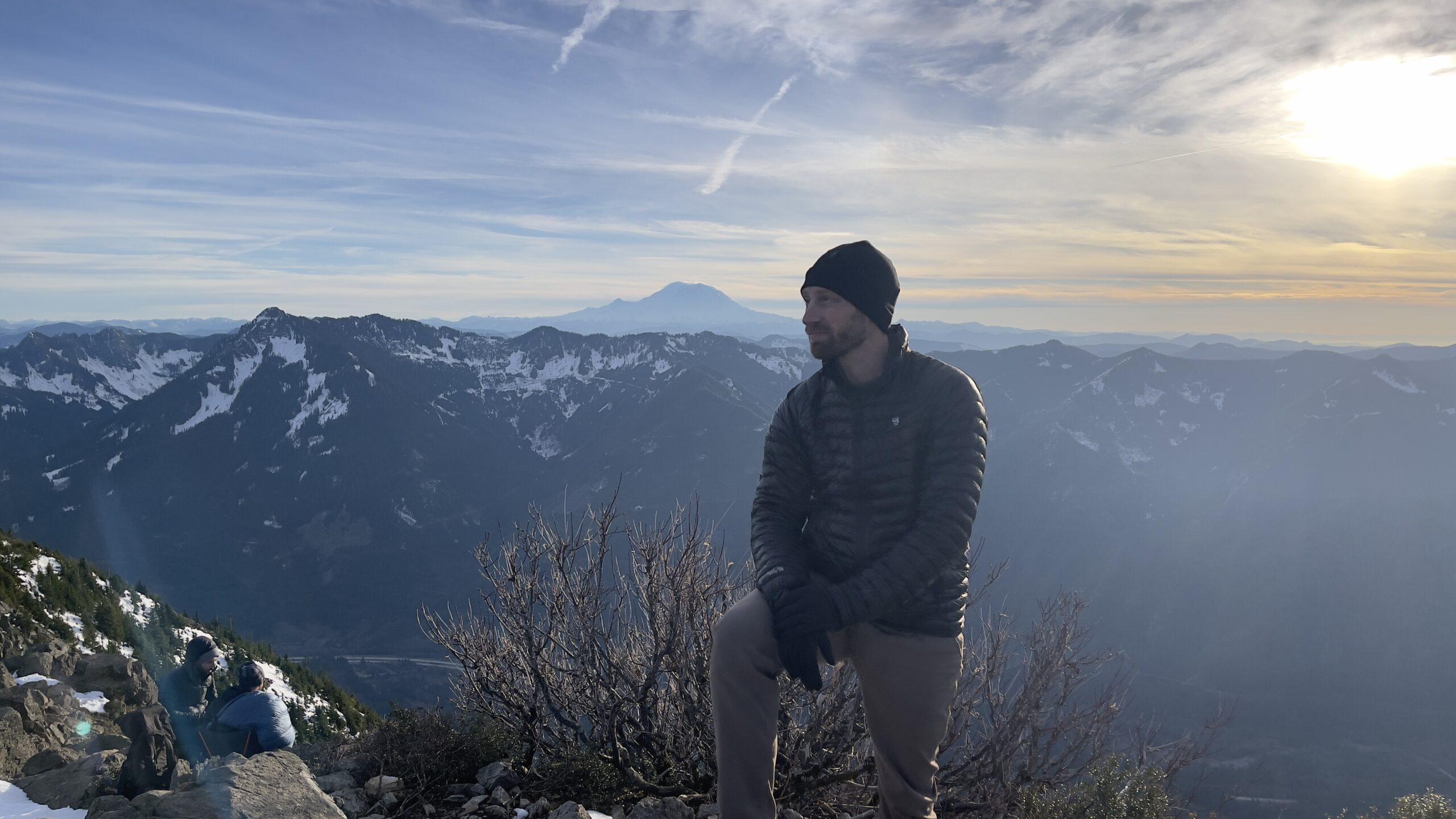 Alex standing at Mailbox Peak with snow peaked Cascade mountains in the background.